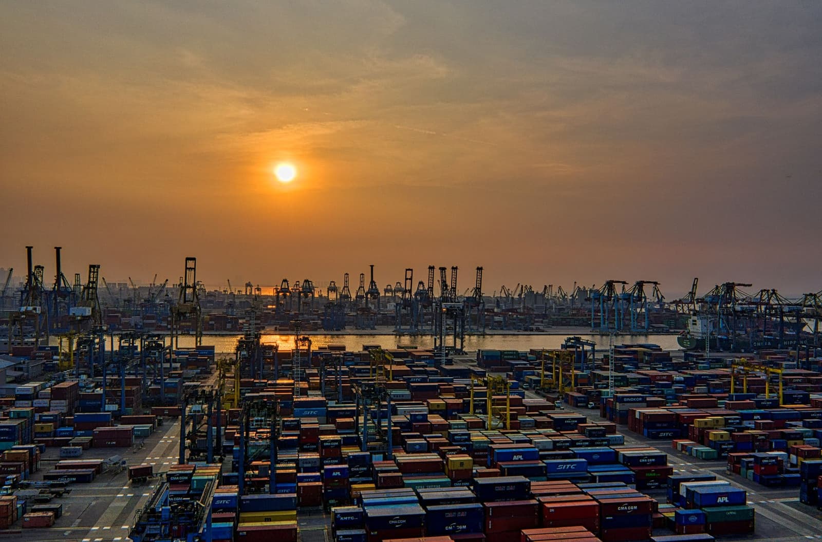 Container terminal at golden hour with stacked cargo and ship-to-shore cranes