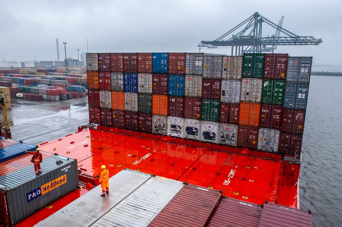 Stacked shipping containers at a busy port under a clear sky